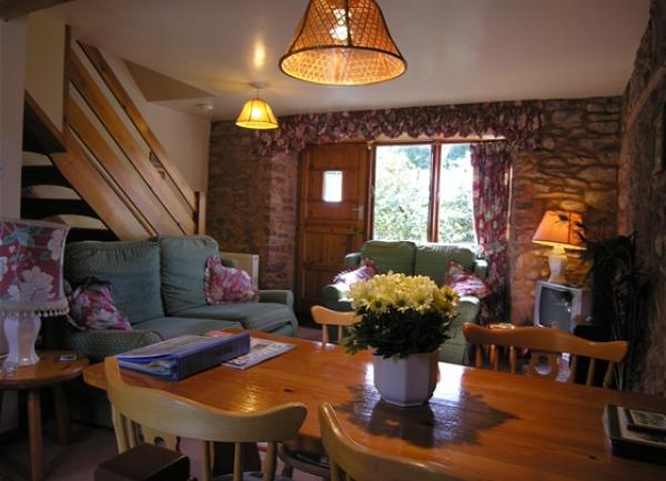 A lounge with exposed stone walls, sofas and a polished wood dining table