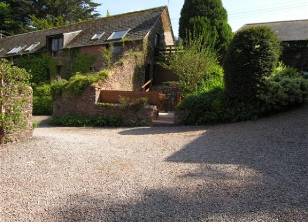 Exterior of a stone barn conversion nestling between small trees and mature shrubs.