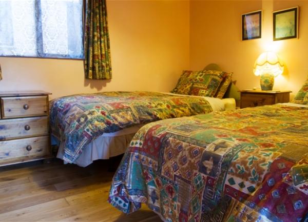 Bedroom with twin beds on pine floorboards with a chest of drawerw.