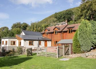 A wooden-clad Shropshire holiday home backed by trees overlooks a lawn backed by trees
