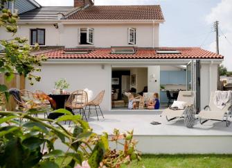 Rear exterior of a 2-story house with floor-to-ceiling sliding doors across the ground floor overlooking a terrace and lawn.