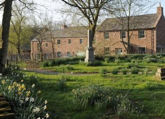 Exterior of a large country house surrounded by lawned gardens.