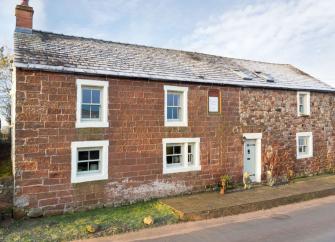 Stone built font exterior of a traditional Cumbrian cottage overlooking a quiet road.