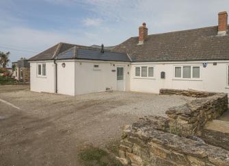 Exterior of a white-rendered holiday bungalow with a large forecourt for parking