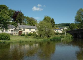 An Exmoor holiday home on the banks of calm river floowing under a stone bridge.