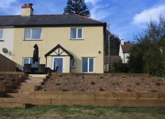 Exterior of a double-fronted house with a patio containing dining furniture