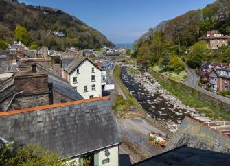 Cottage window view of a rocky river flowing through a village in a valley.