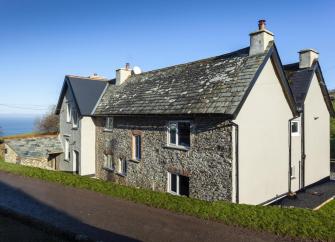 Exterior of a twin-gabled Exmoor Farmhouse set back from a country lane and surrounded by open fields with a distant sea view.