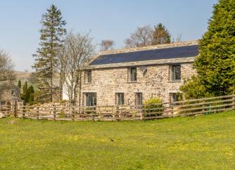 Exterior of a stone-built barn conversion overlooking a field.