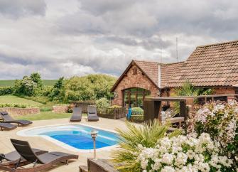 A stone barn conversion overlooks an outdoor swimming pool in a shrub-filled garden