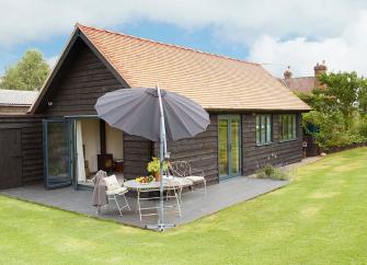 A single-storey clapperboard barn conversion with a patio and well-kept lawn.