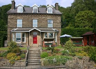 Exterior of a stone-built, 3-storey detached house  in front of a wood and overlooking a terraced garden