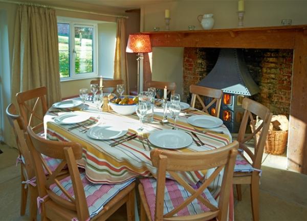 A dining room with inglenook fireplace and table laid for 8 guests.