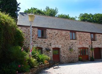 A stone-built, 2-storey courtyard cottage with foxgloves flowering in its garden.