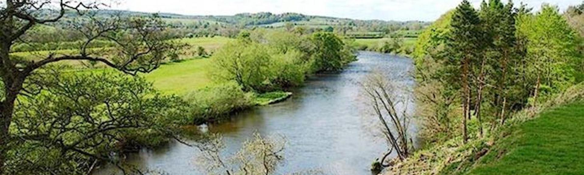 A wide tree-lined river winds through the Cumbrian Countryside near Glassonny