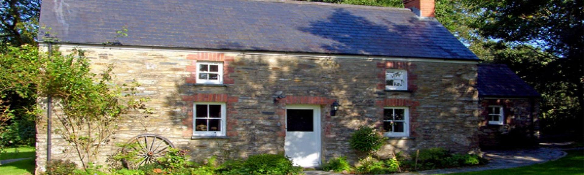 The exterior of  stone-built Welsh farmhouse overlooking  lawn with tall tree to its side and rear. an old cart wheel leans against the wall of the house.