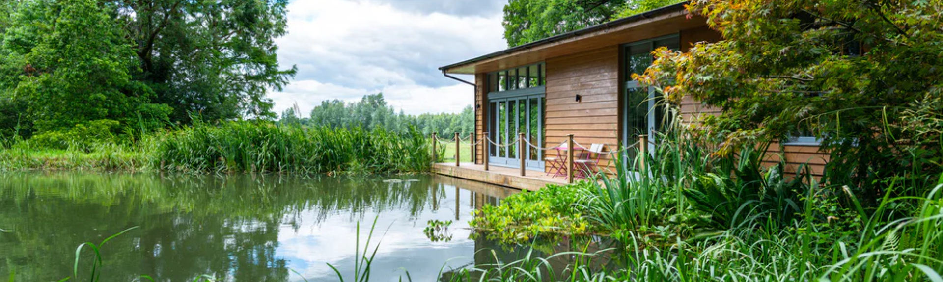 A wooden holiday lodge looks out across a reed-fringed river in Hampshire