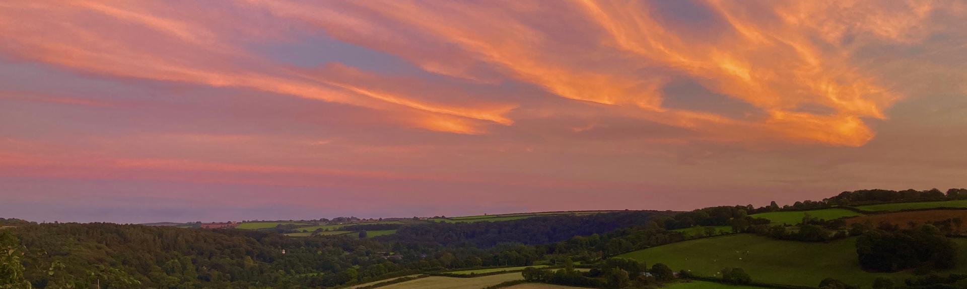 cloudes reflect the setting sun over a summer hillside ladscape of Devon fields
