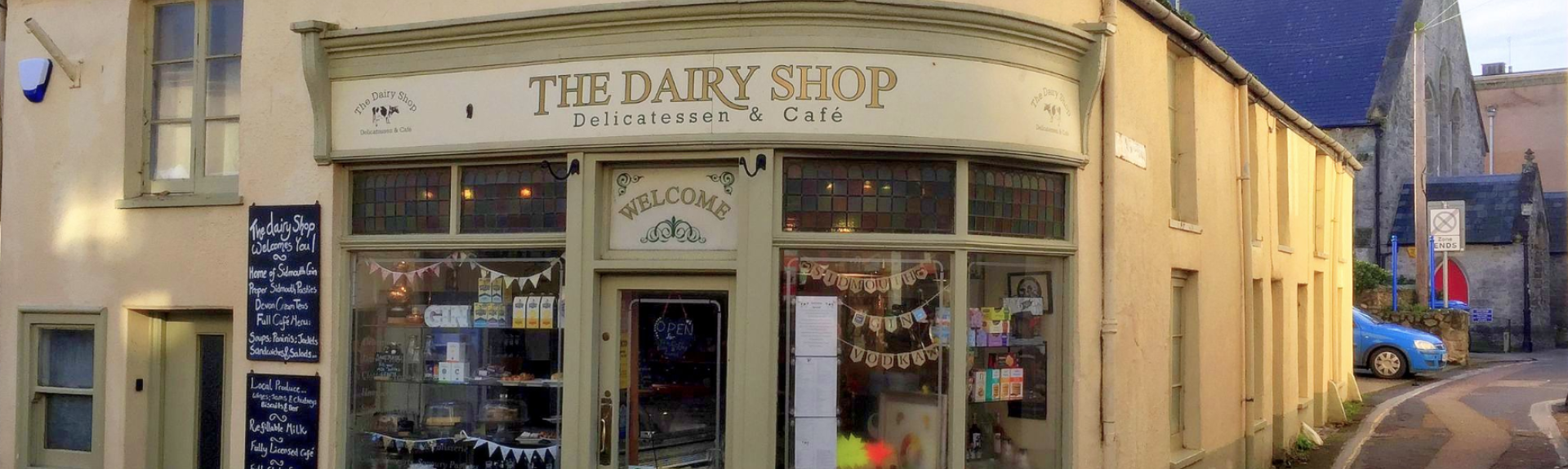 The shop front for The Dairy Cafe in Sidmouth with large windows displaying local produce.