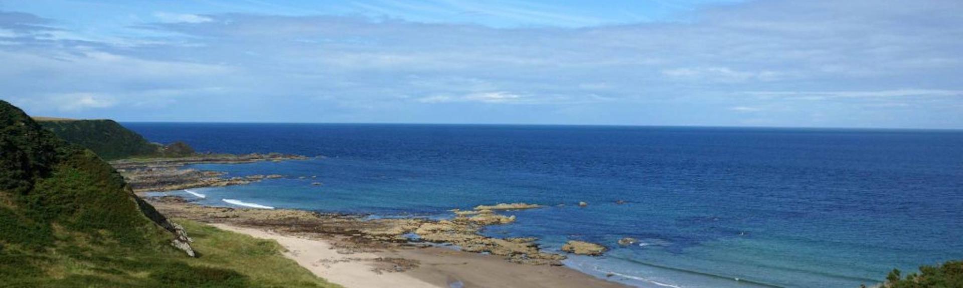 View of low grassy hills sloping down to a small beach in Banff, Aberdeenshire
