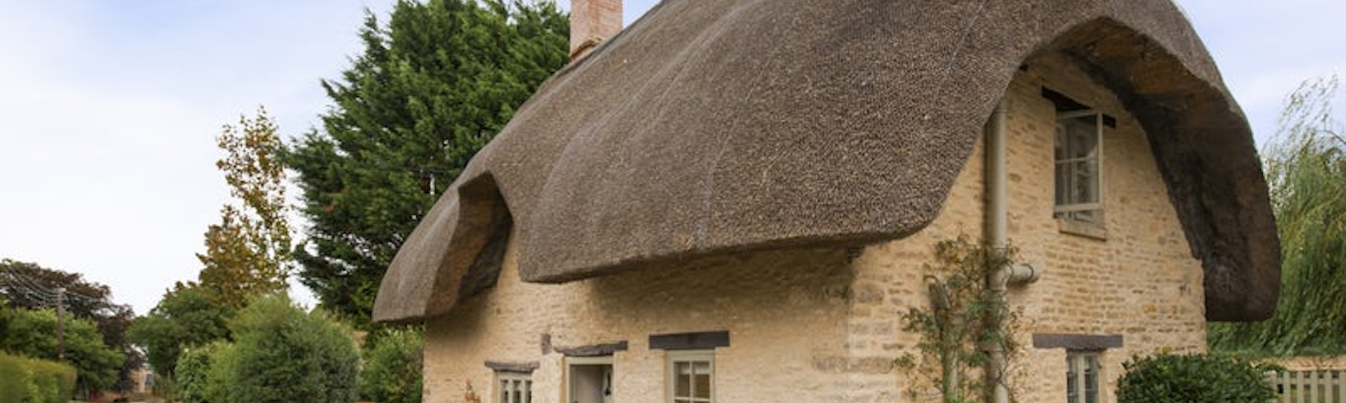 A thatched country cottage overlooks a quiet country lane in the Cotswolds.