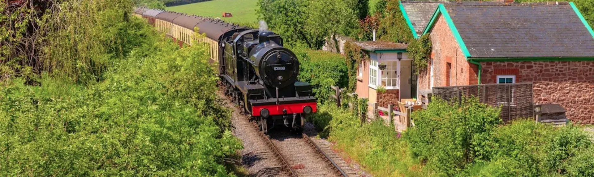 A restored Great Western Tank Engine steams past a holiday cottage in the West Somerset countryside.