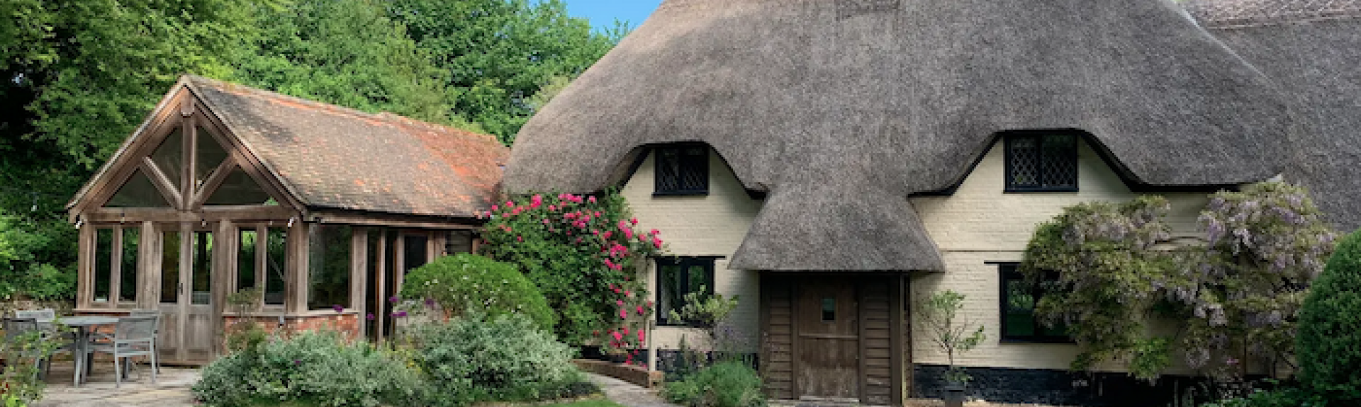 A thatched holiday cottage in Blandford Forum with a slate-roofed extension overlooks a well-kept lawn