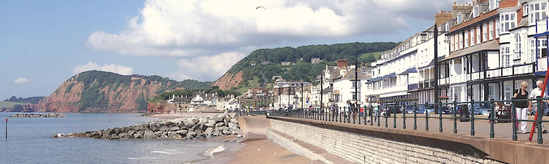 An esplanade lined by cafes and hotels overlooks a shingle beach in East Devon.
