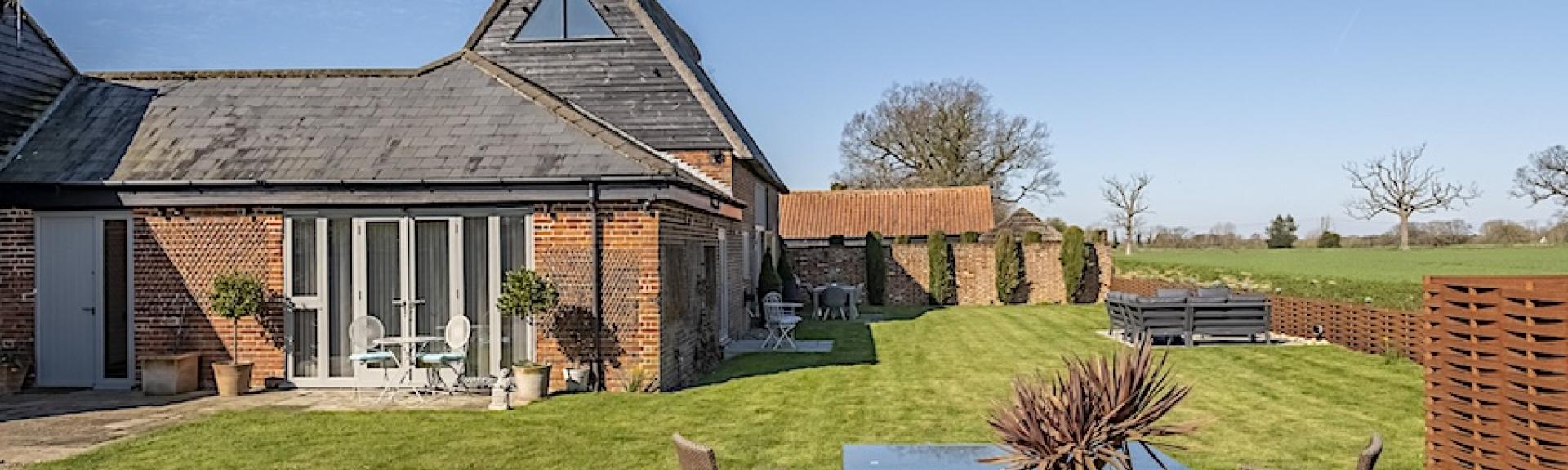 A partially thatched barn conversion overlooks spacious, fenced lawns with an outdoor dining area.