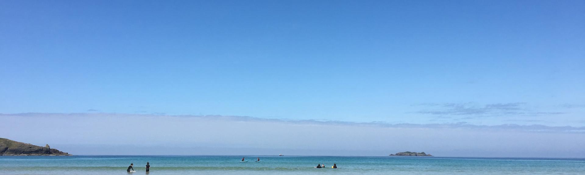 A Cornish sandy beach at low tide beneath a clear summer sky.