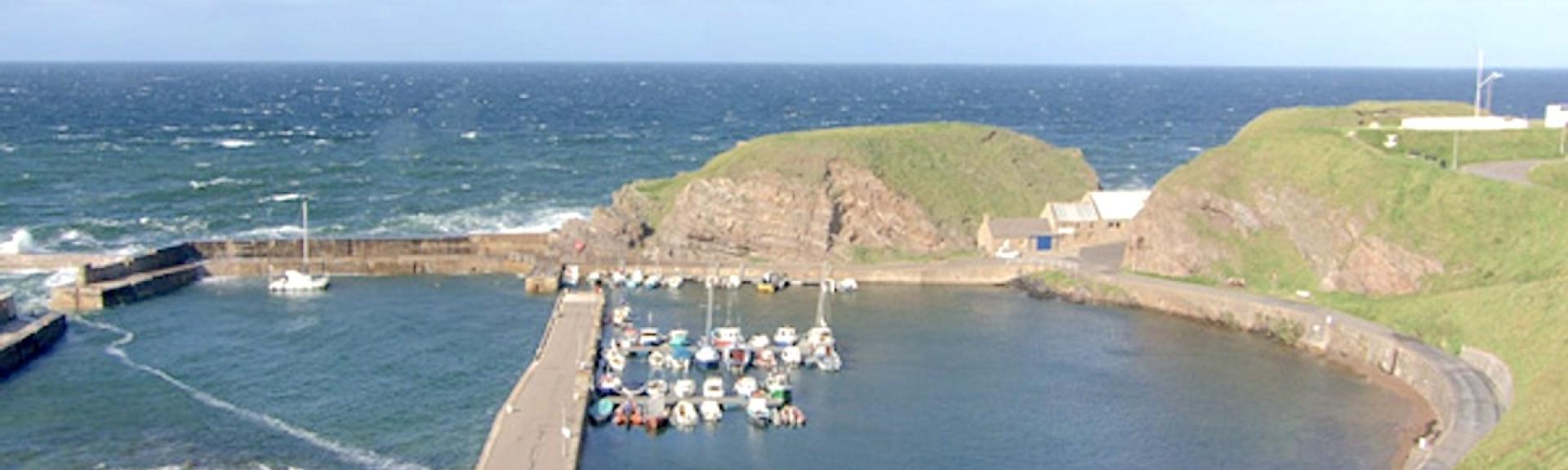 Aerial view of a Scottish harbour with small fishing boats in a natural cove.