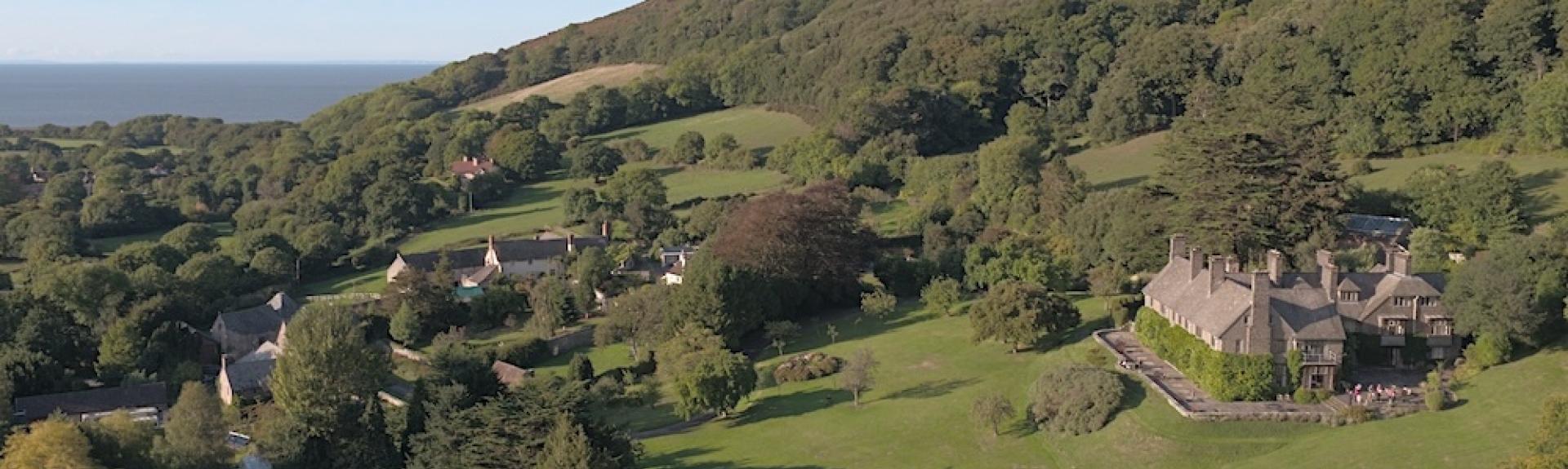 An aerial view of a small hamlet nestling beneath a tree and bracken covered Moorland hill top.