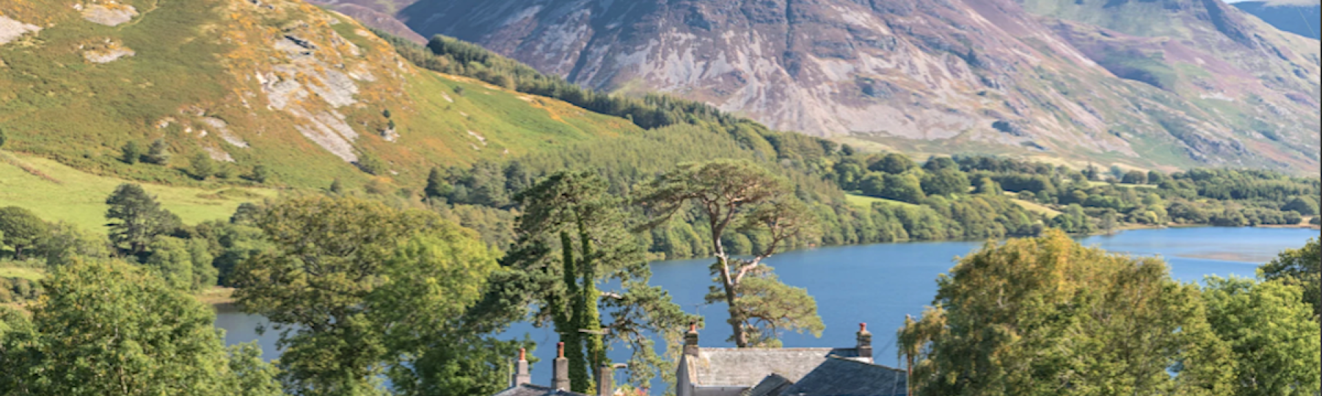 A holiday cottage overlooks a large lake in front of tall Lake District Fells.