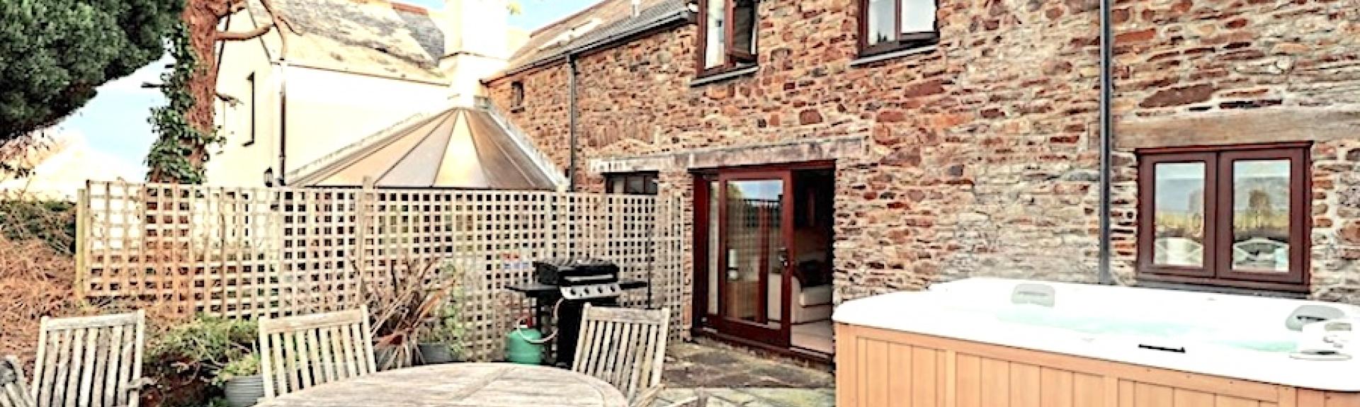 A holiday cottage courtyard with a hot tub, outdoor dining table and chairs