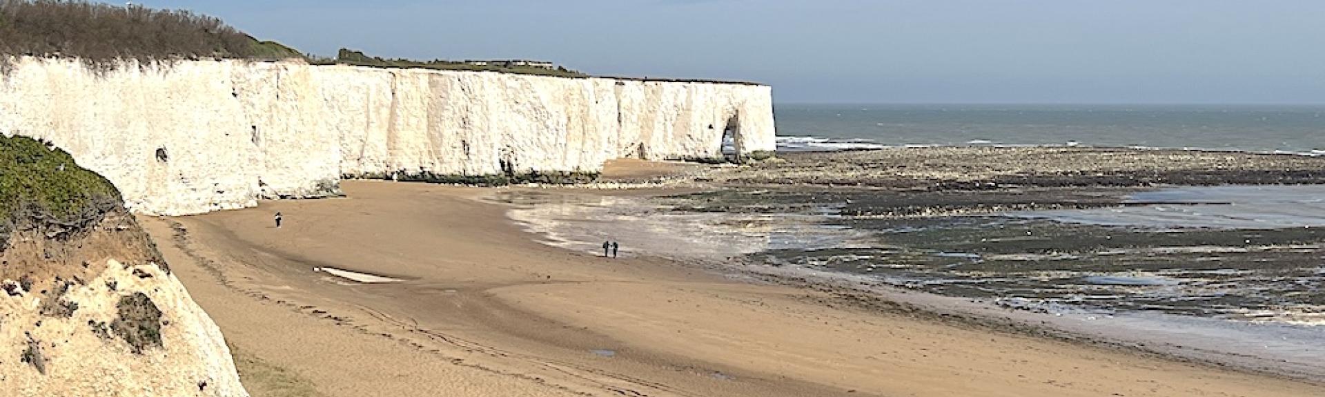 White cliffs at Broadstairs tower above a sandy beach at low tide on a clear summer's day.