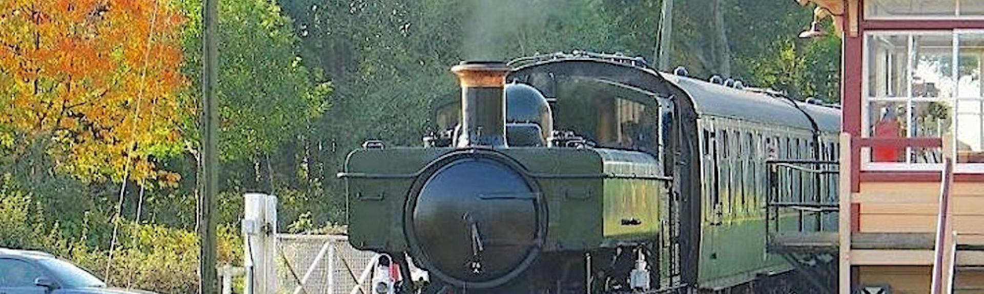 A pannier tank steam engine heads a train through s level crossing in Wittersham