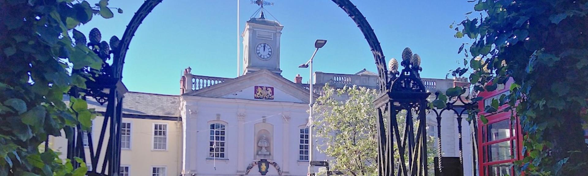 A town hall with a clock tower seen  through an ornate ironwork arch