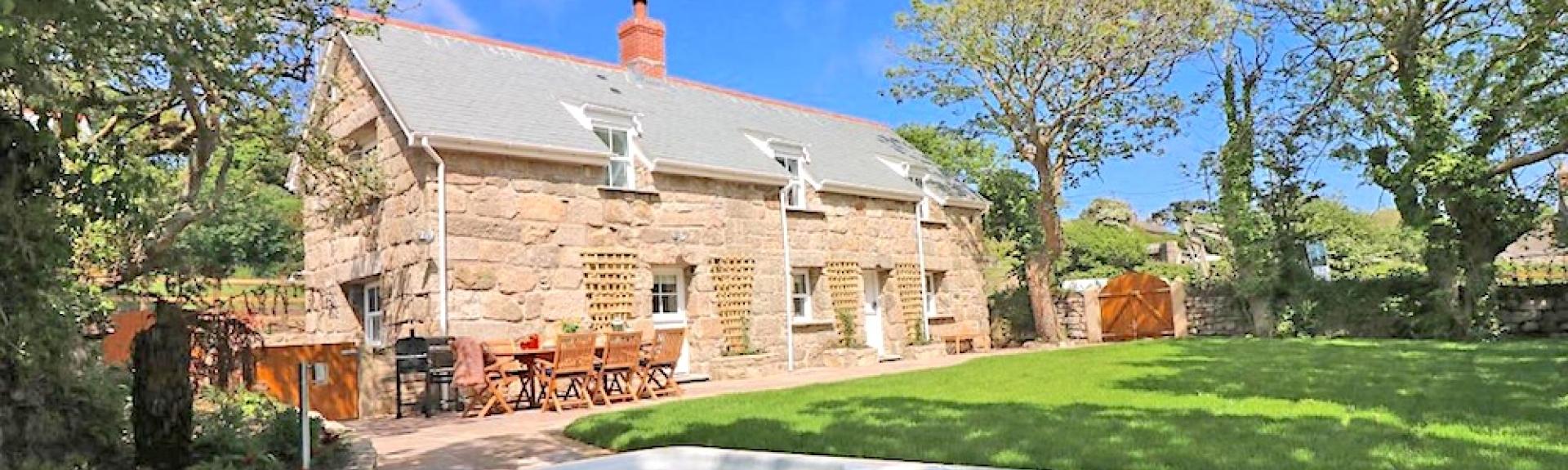A large Cornish cottage overlooks a tree-lined lawn lawn with a hot tub.