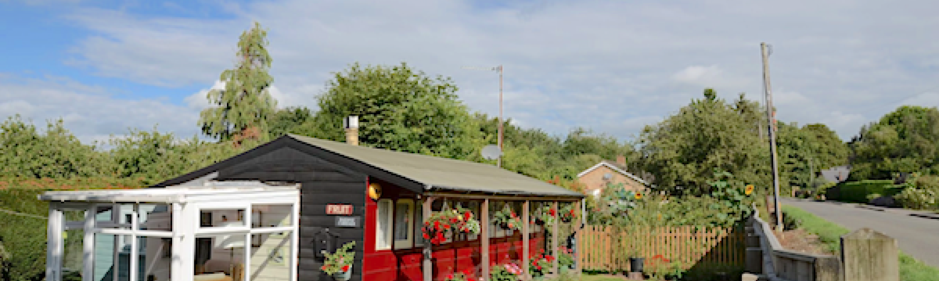 A restored old railway carriage converted to a self-catering holiday home festooned with flowers stands in a well-kept garden in Wisbech on a sunny day