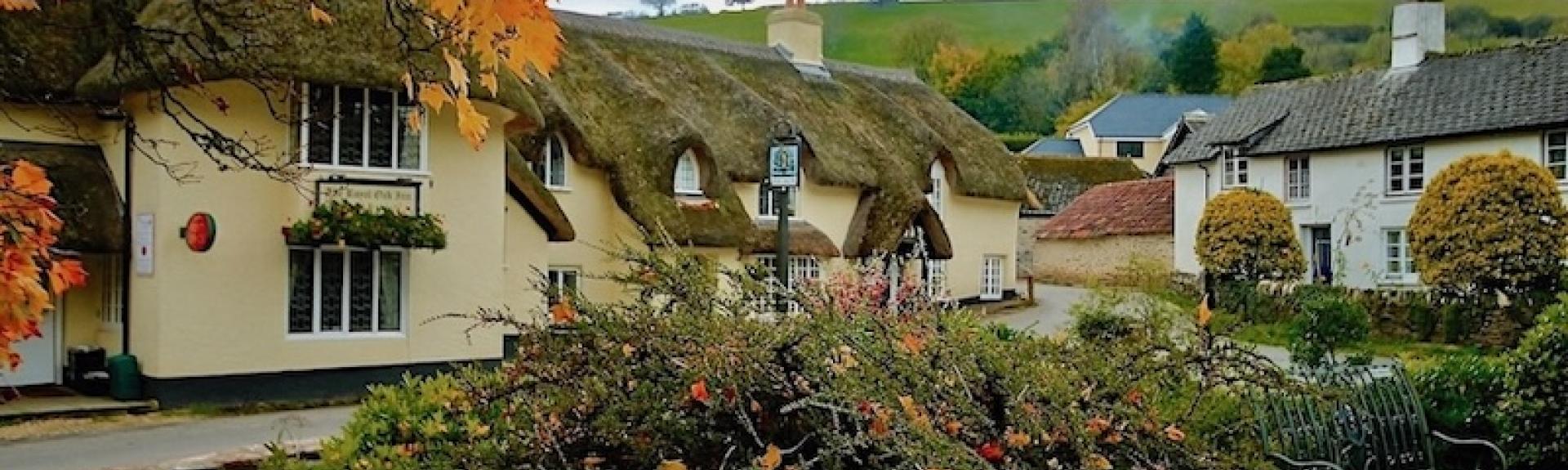 A large thatched Exmoor pub in Winsford is surrounded by trees and bushes in autumn colours.