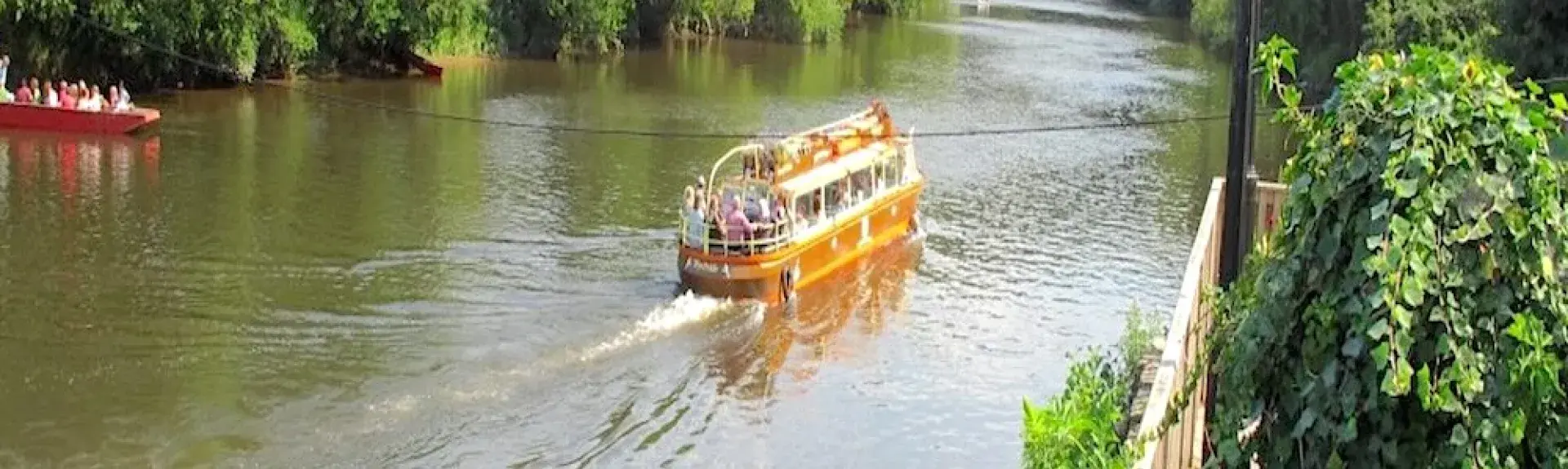 Boats on the River Wye cruise through a wooded section of the Wye Valley.