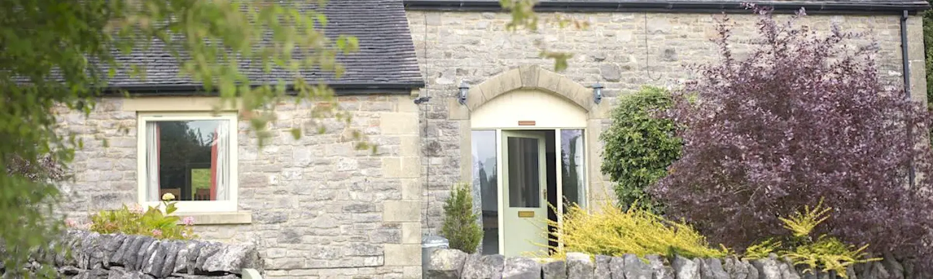 A gate in a stone wall leads up a garden path to the entrance of a stone-built cottage