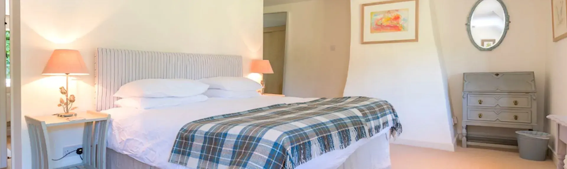 A spacious Bridport holiday cottage bedroom with a large double bed, tartan bedspread and carpeted floor.