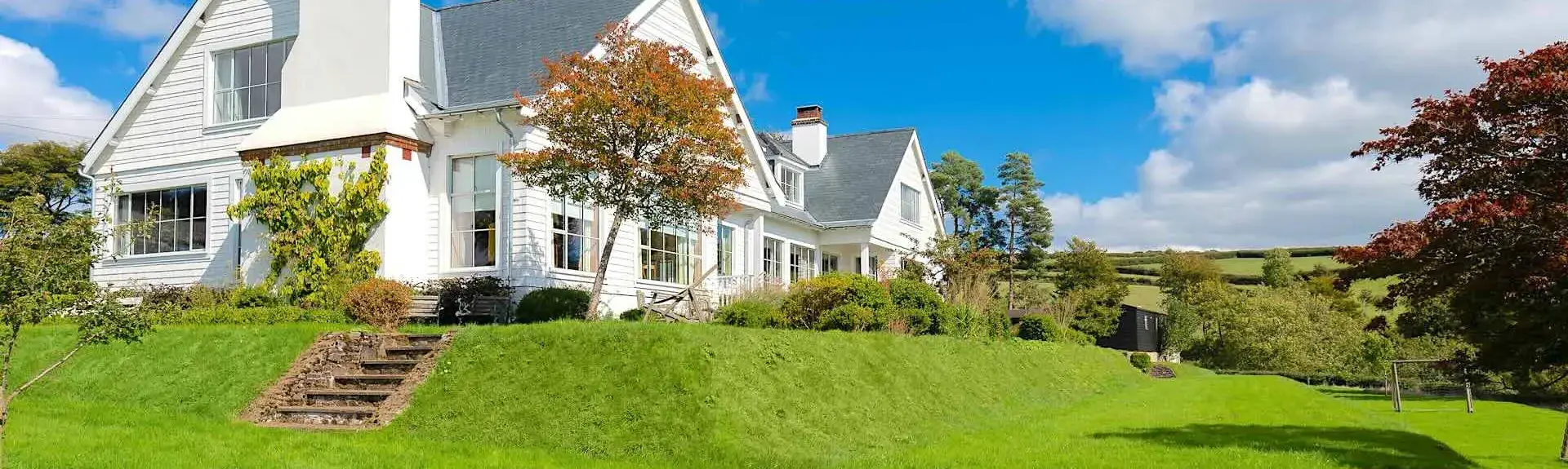 A long, clapper-boarded Exmoor house with twin gables overlooking a large tree-lined lawn.