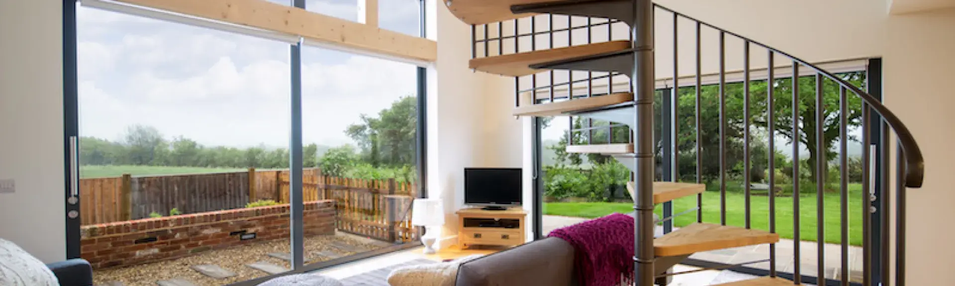 A. holiday cottage lounge with floor-to-ceiling windows, sofas and a spiral staircase