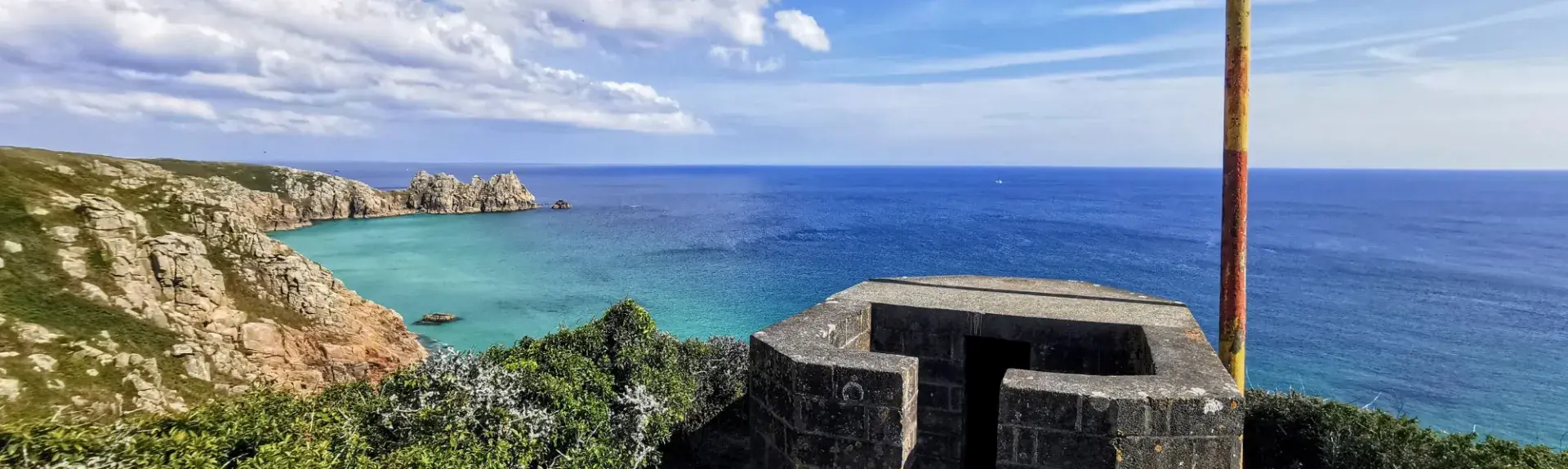 A clifftop view of turquoise and blue sea with blue skies and clouds.