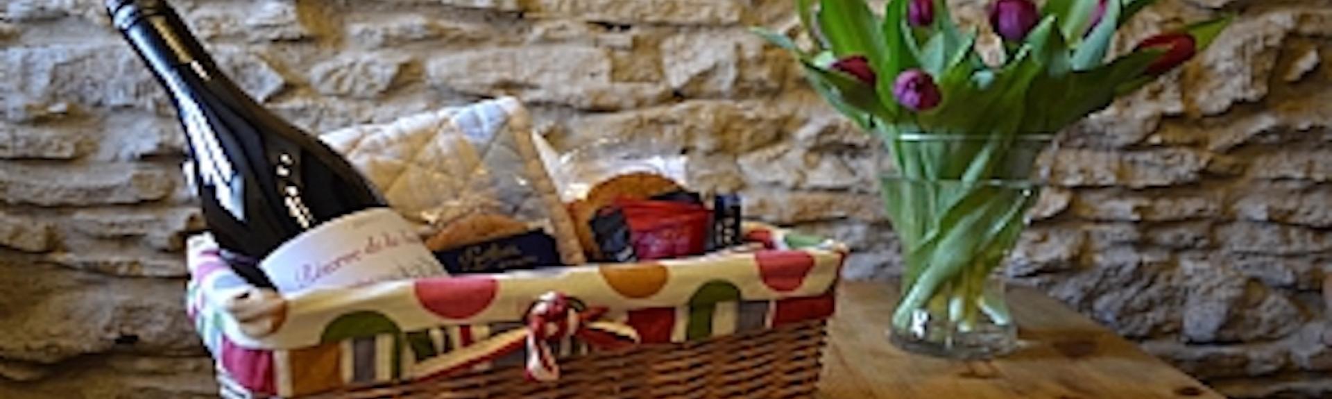 A North Yorkshire holiday cottage welcome basket stocked with goodies - bread, wine, jam, biscuits sits on a table. 