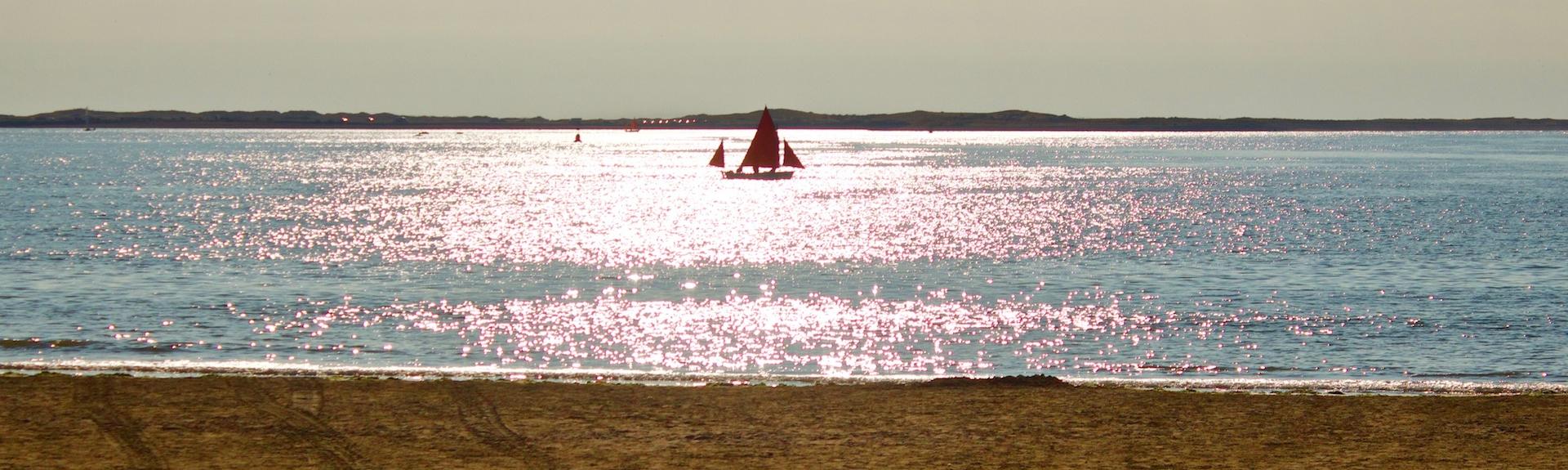 A sailing boat silhouetted against sunlit waves off Instow Beach in North Devon 