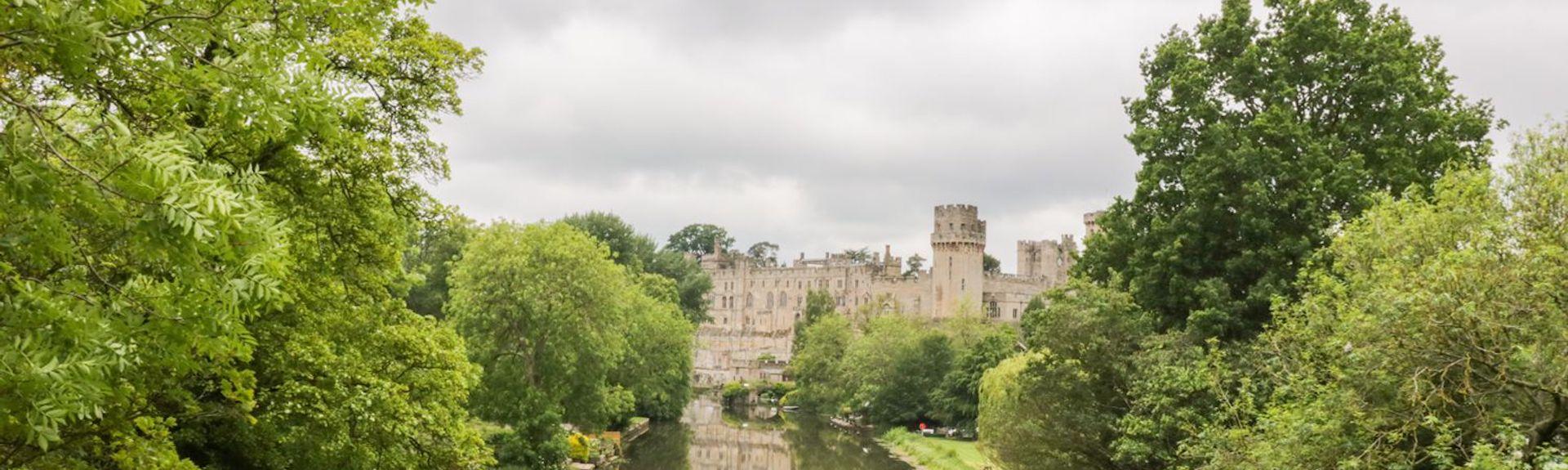 The wide River Avon flows placidly between tree-lined banks towards Warwick Castle 
