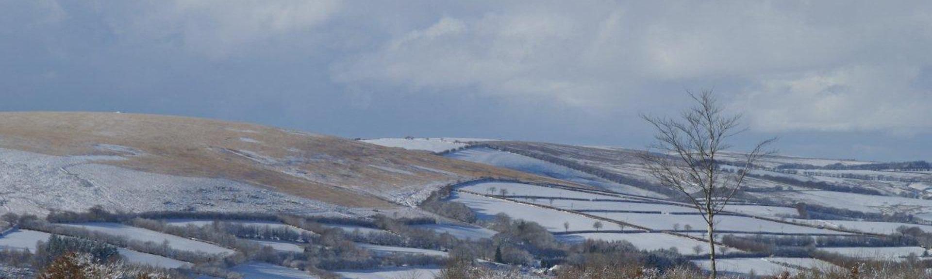 A winter view of a snow-covered Exmoor landscape which lies beneath dark, snow-laden clouds